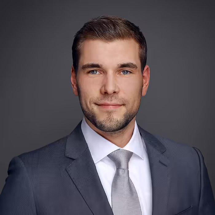 Bewerbungsfoto eines Mannes im grauen Anzug mit Krawatte vor neutralem Hintergrund
